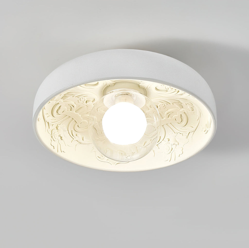 Clérachic bowl light lit with a clear glass globe, its carved interior glowing warm cream against a pale grey ceiling.