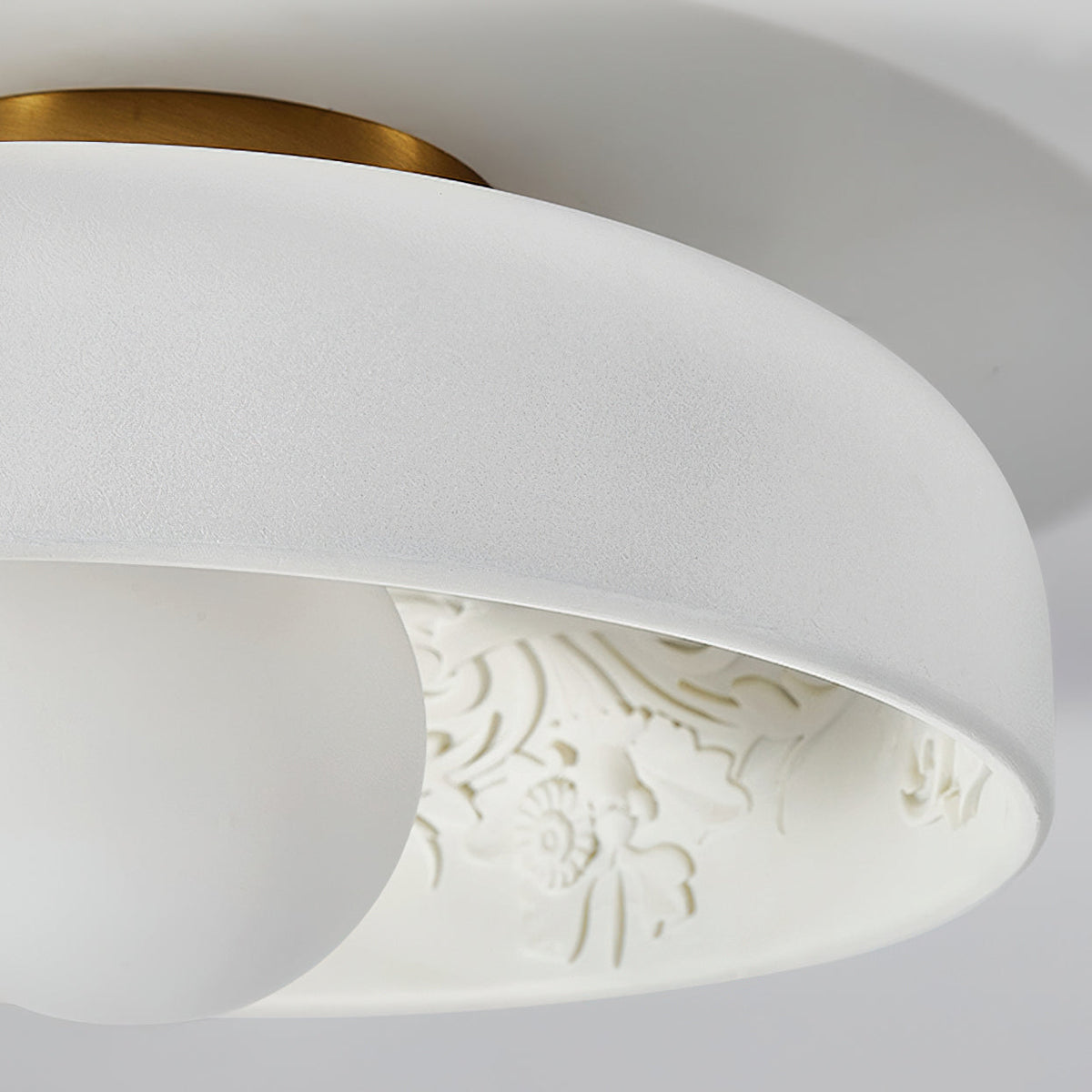 Close view of the textured white rim, brass canopy and white globe on this Clérachic carved-resin ceiling light.