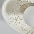Close-up of the carved scrolls and small flowers inside this Clérachic bowl light, with the white globe at the edge.