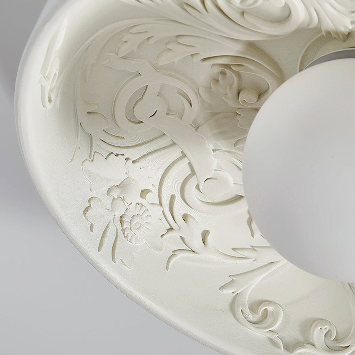 Close-up of the carved scrolls and small flowers inside this Clérachic bowl light, with the white globe at the edge.