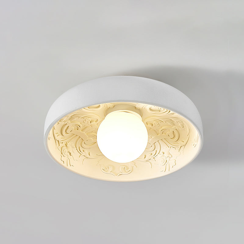 Clérachic carved-resin ceiling light switched on, with a warm cream glow inside the bowl and a round frosted globe.