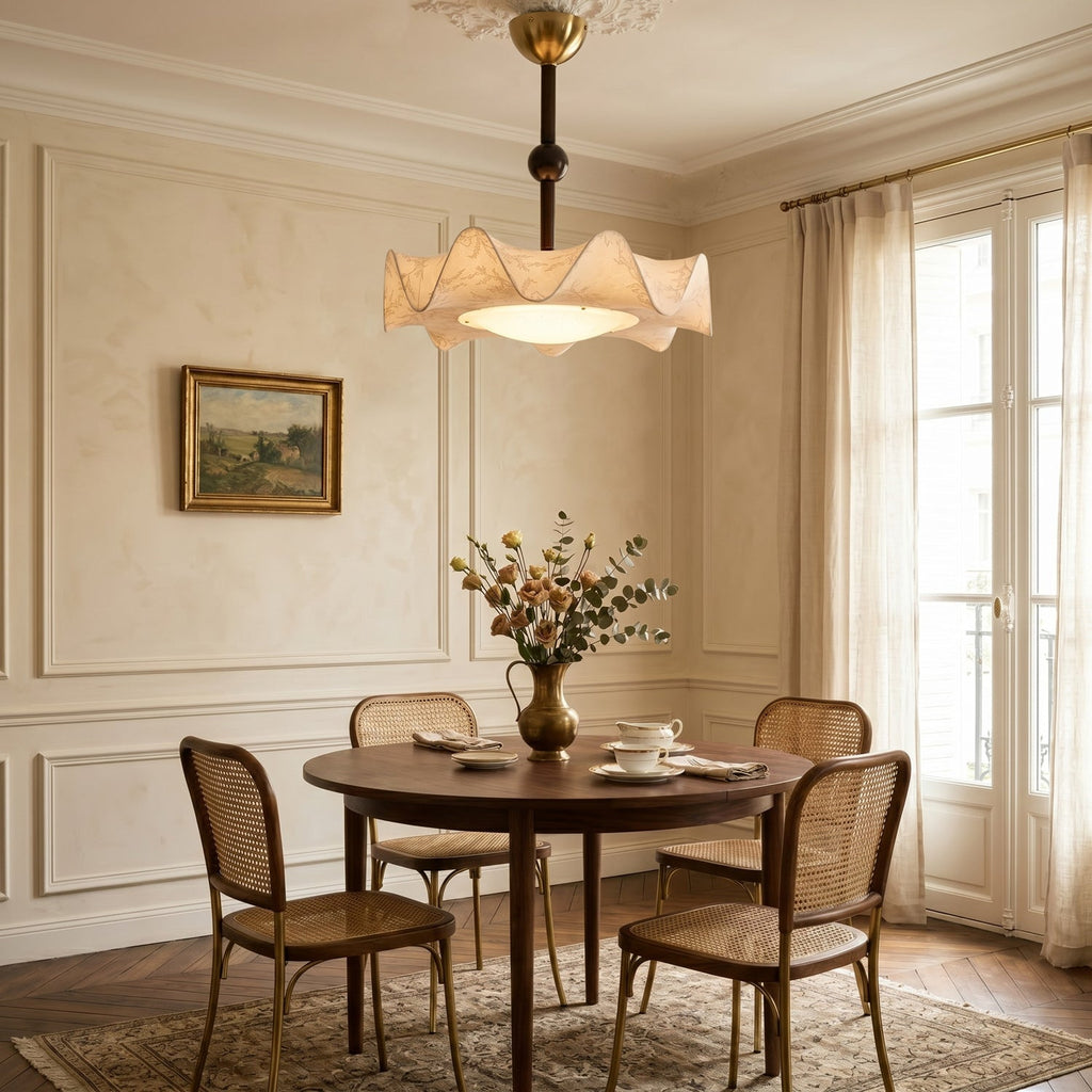 A Clérachic ceiling light with a ruffled shade, lit above a round wooden dining table with cane-back chairs in a panelled room.