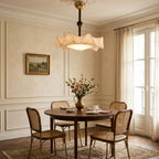 A Clérachic ceiling light with a ruffled shade, lit above a round wooden dining table with cane-back chairs in a panelled room.