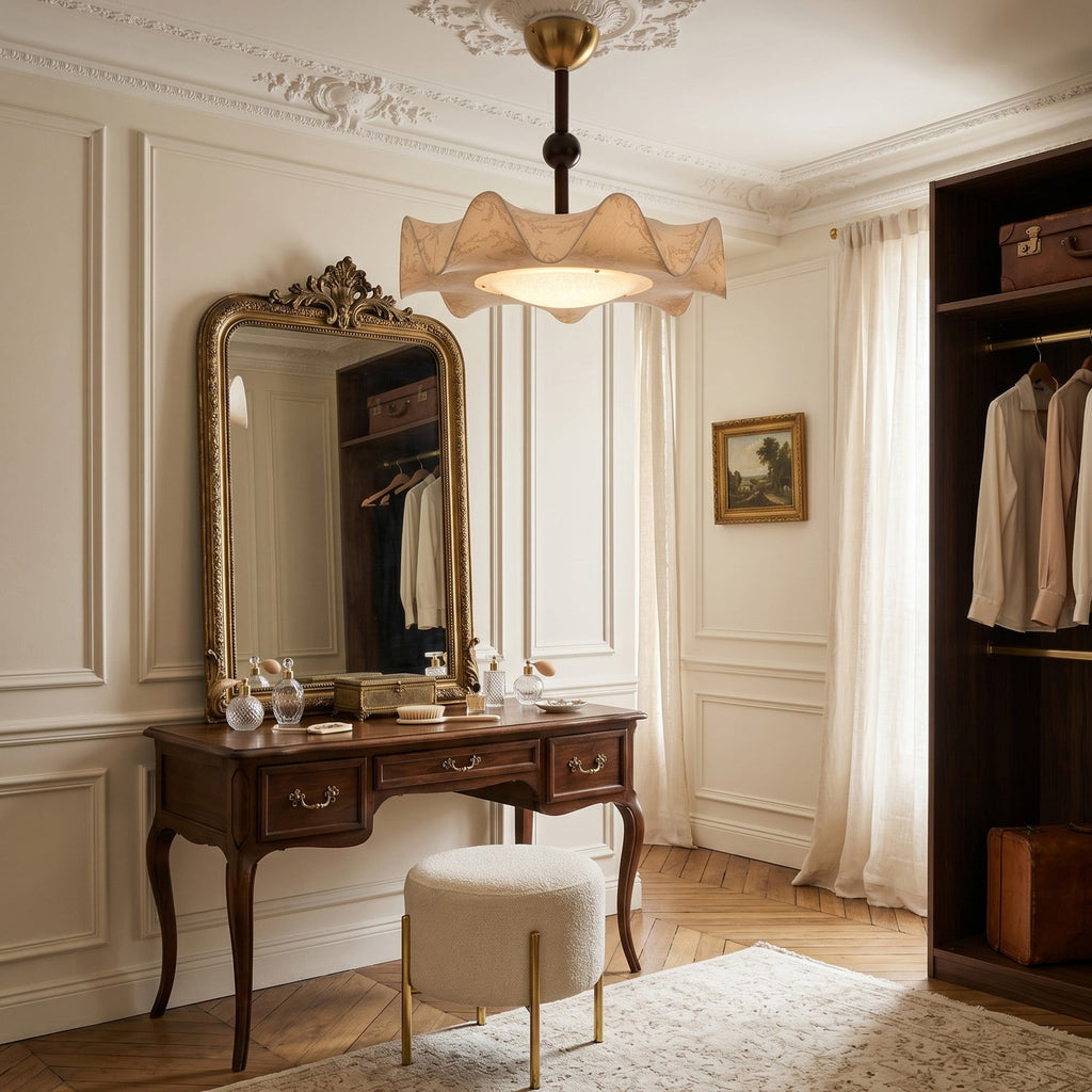 Clérachic ceiling light above a dressing room with a carved vanity table, a gilt mirror and a wardrobe of hanging shirts.