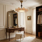 Clérachic ceiling light above a dressing room with a carved vanity table, a gilt mirror and a wardrobe of hanging shirts.