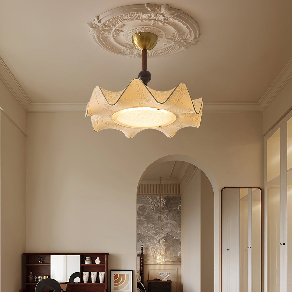 A Clérachic ceiling light with a wavy cream shade, lit under a plaster ceiling rose, with an arched doorway and a dressing table behind.