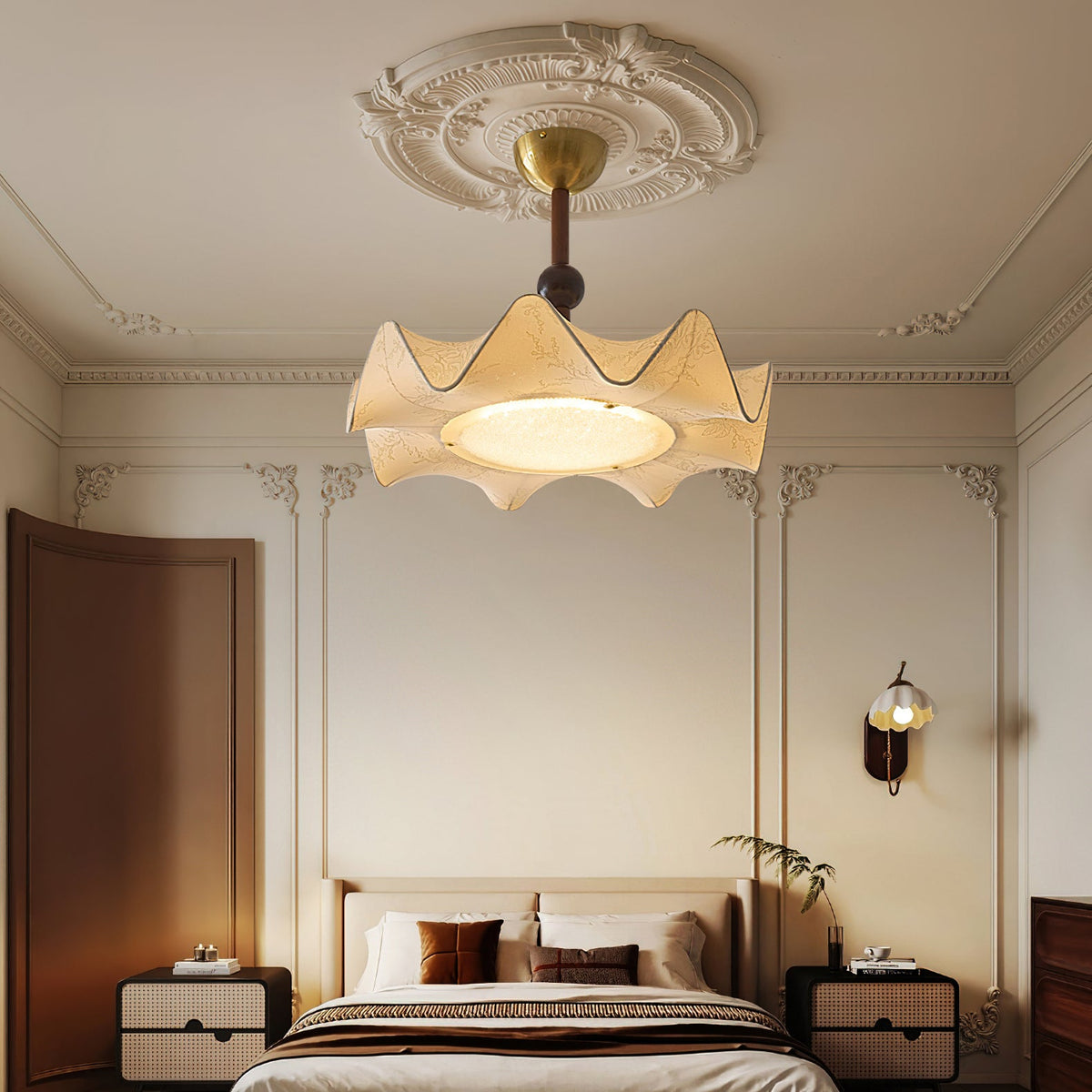 A Clérachic ceiling light hangs in a bedroom with ornate wall mouldings, above a bed with cane-front bedside tables.