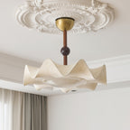 Close view of the brass canopy, walnut-toned stem and wavy edge of this Clérachic ceiling light, under a plaster ceiling rose.