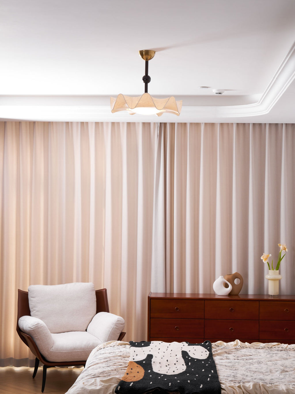 A Clérachic ceiling light hangs in a room with peach curtains, a white armchair and a dark wood chest of drawers.