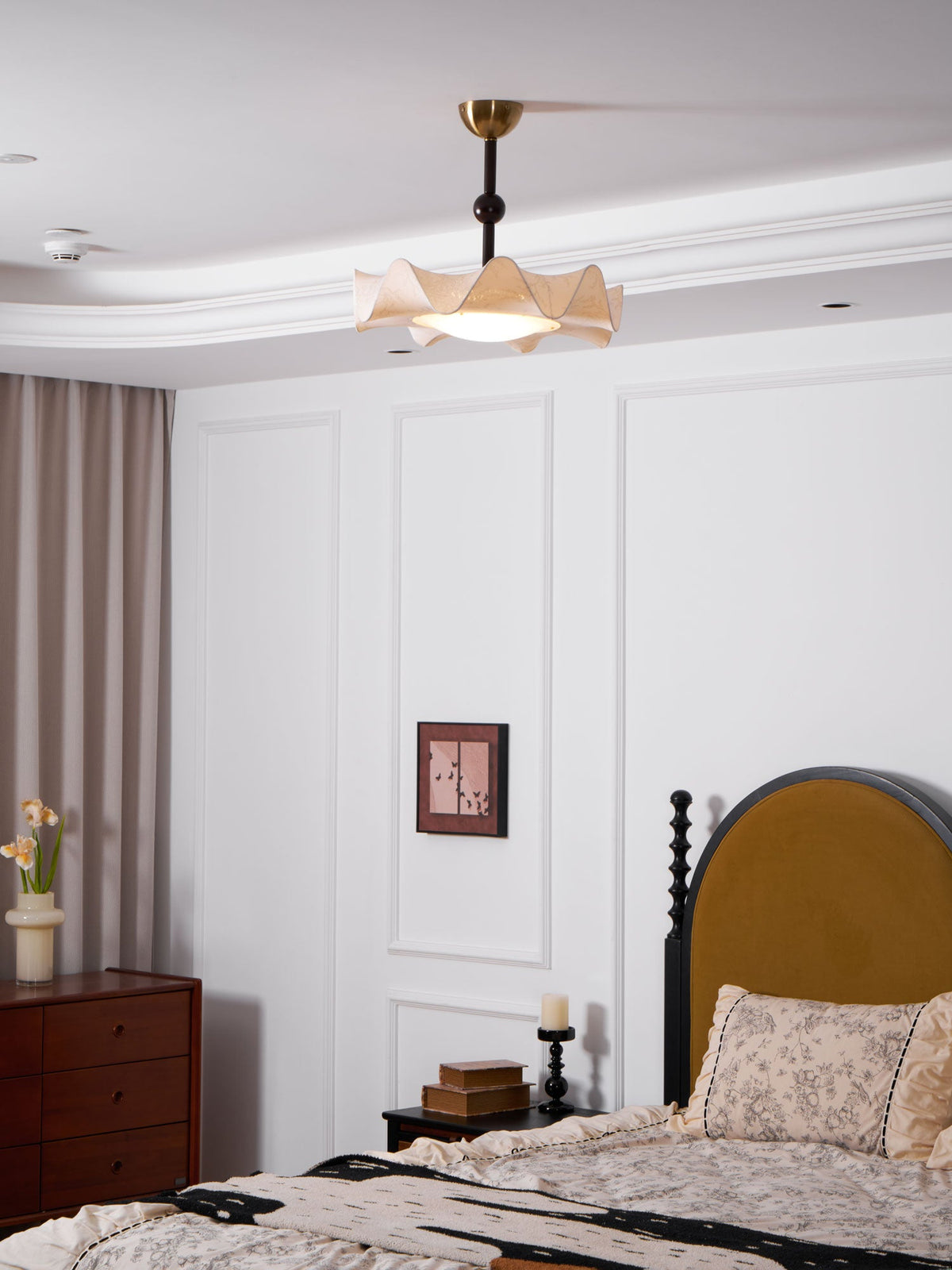 Clérachic ceiling light on a white-panelled ceiling above a bed with a mustard headboard and a patterned throw.