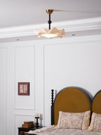 The Clérachic ceiling light seen from another angle, above a bed with a mustard headboard and a framed print on the wall.