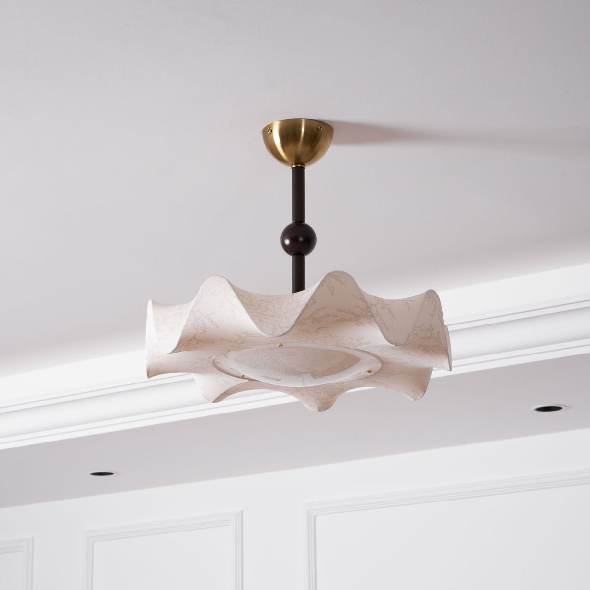 Angled view from below of this Clérachic ceiling light, with its wavy shade, round diffuser and a dark ball on the stem.