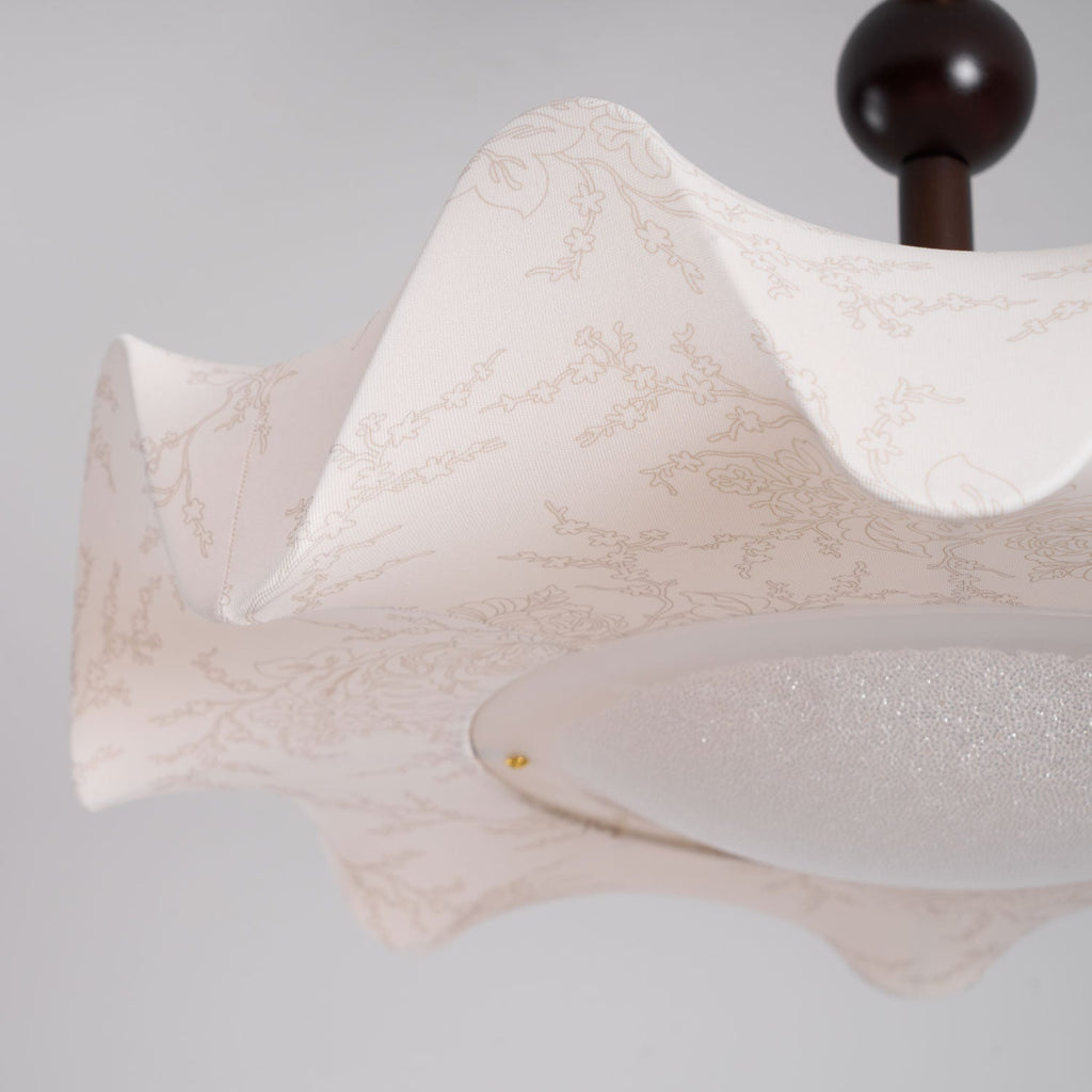 Close view of the wavy fabric edge and the speckled diffuser on this Clérachic ceiling light, with its dark wooden ball above.