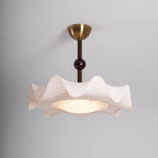 Lit Clérachic ceiling light against a grey ceiling, showing the brass canopy, slim stem and a warm glowing diffuser.