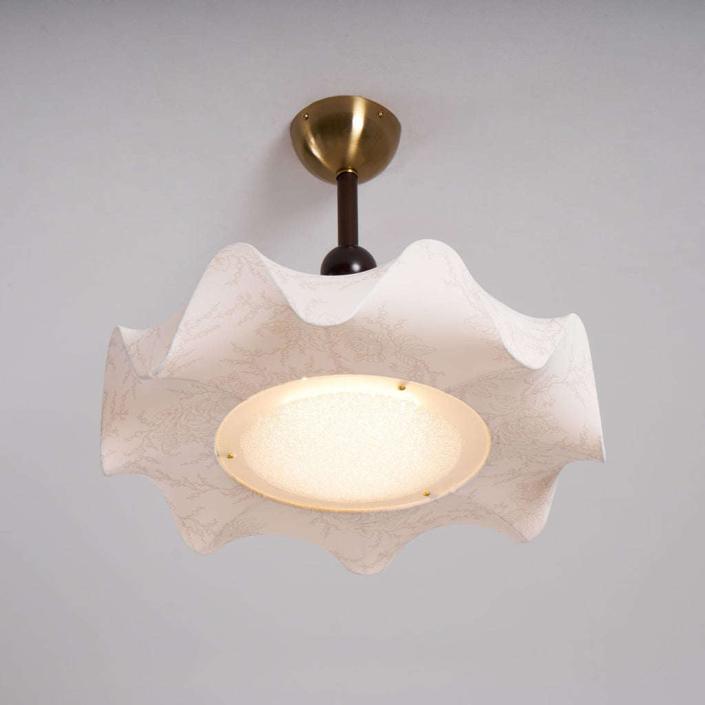 Straight view of this lit Clérachic ceiling light, with a brass canopy, a walnut-toned stem and a ruffled shade around the glow.