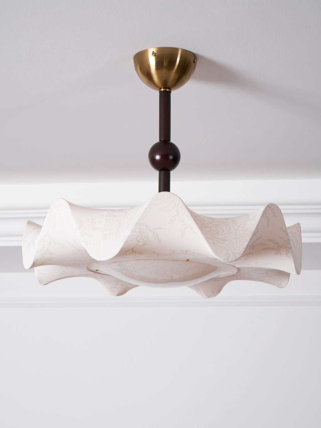 A Clérachic ceiling light below a ceiling cornice, with its wavy shade and a round diffuser seen from underneath.