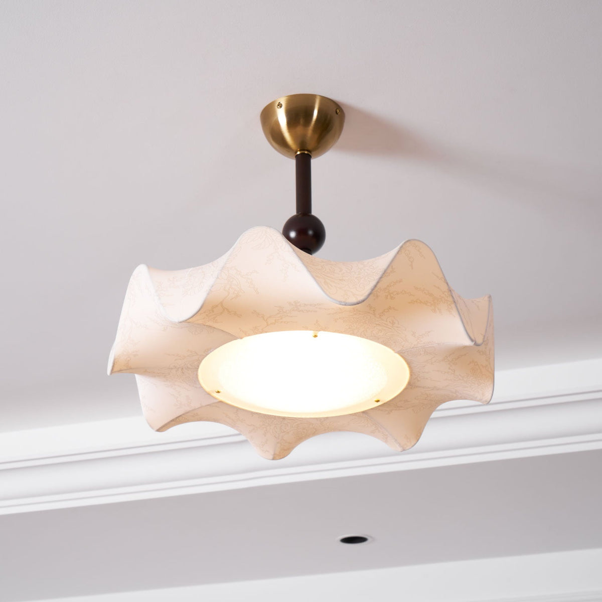 Lit Clérachic ceiling light beside a white cornice, with the diffuser shining warm inside the ruffled shade.