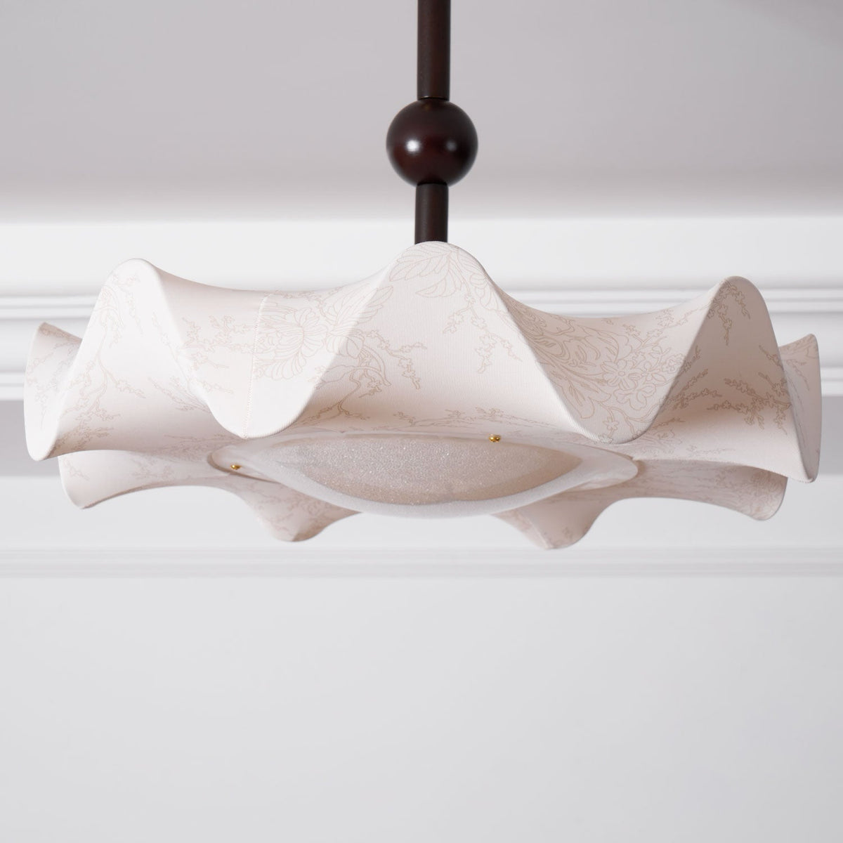 Wide view of the wavy shade on this Clérachic ceiling light, with the stem and dark ball above, under a white cornice.