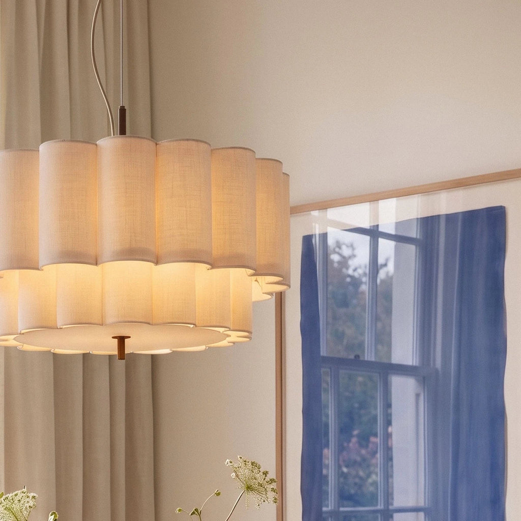 A Clérachic pendant light's scalloped fabric tiers glow beside sheer curtains and a framed blue window print.