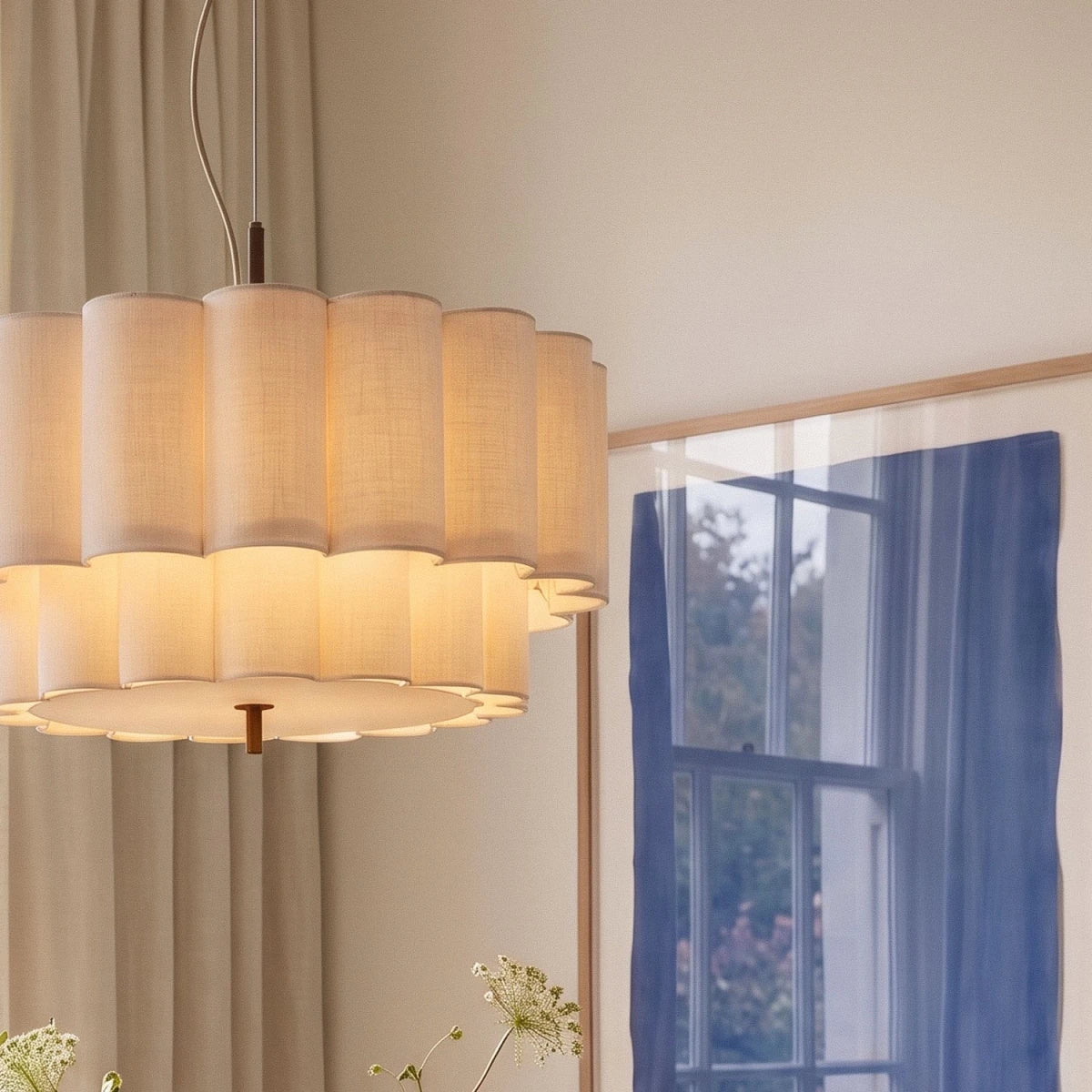 A Clérachic pendant light's scalloped fabric tiers glow beside sheer curtains and a framed blue window print.