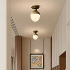 Two Clérachic ceiling lights with brass tops and white glass globes hang along a cream hallway with tall white cabinets and a framed abstract print.