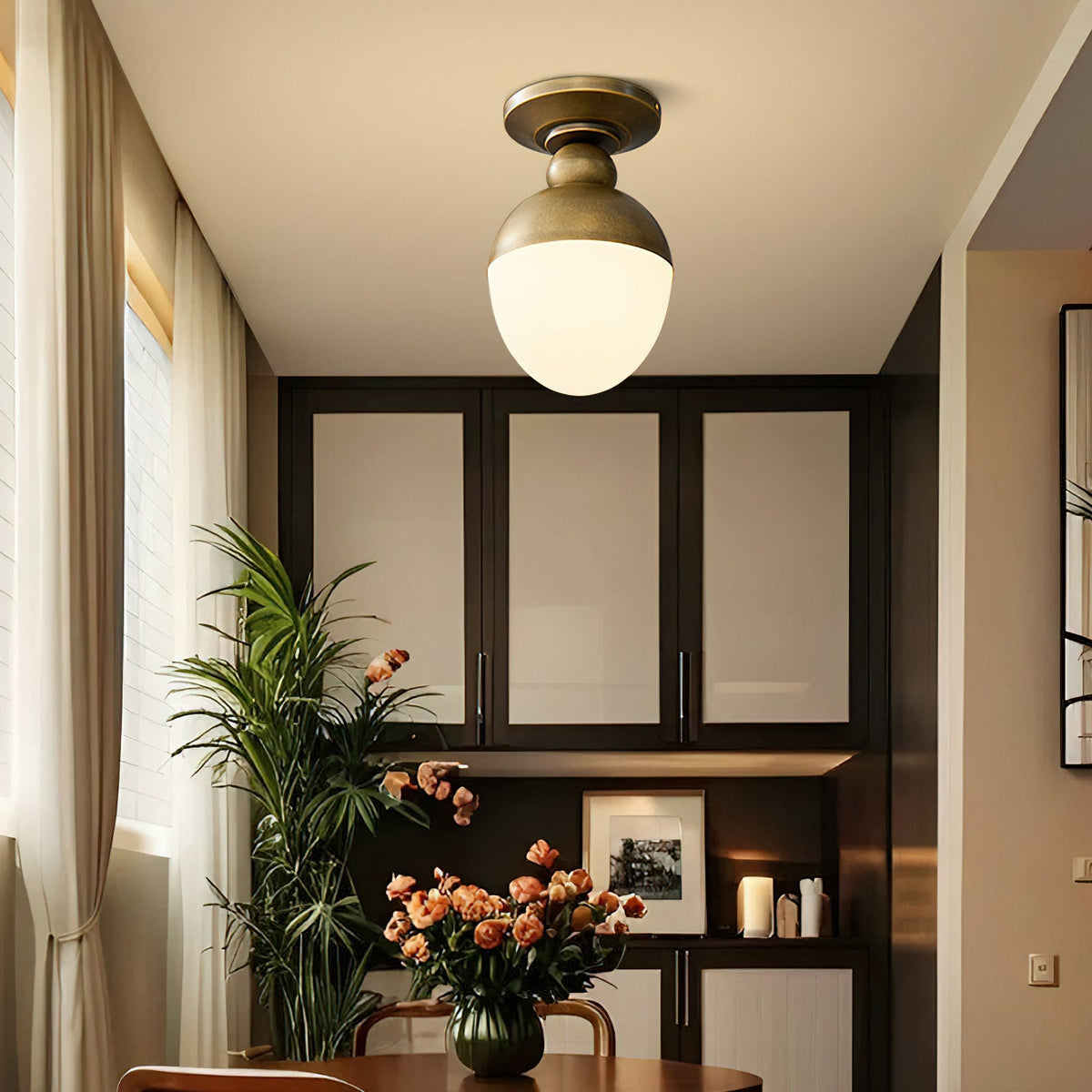 Lit white glass globe with an antique brass top on this Clérachic ceiling light, above a dining corner with a leafy plant and orange flowers.
