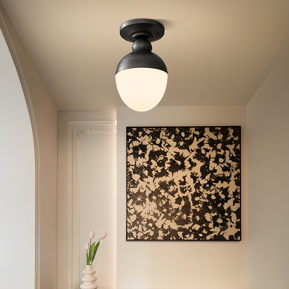 This Clérachic ceiling light has a black top and a glowing white globe, set in a cream room before a large black-and-white abstract artwork.