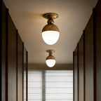 Two antique brass ceiling lights with glowing white globes run down a dark wood-panelled corridor, a pair of Clérachic fittings.