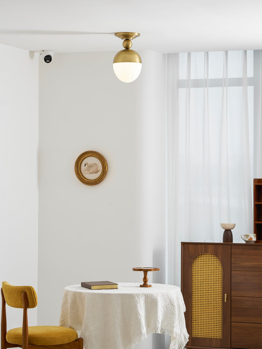 Seen from across a bright room, this Clérachic ceiling light glows white under a brass top, with a round framed picture on the wall behind.