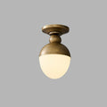Lit antique brass and white glass ceiling light from Clérachic, its globe glowing warm, against a plain grey backdrop.