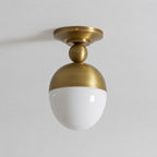 Close, straight-on view of the antique brass canopy, ball joint and unlit white glass globe of this Clérachic ceiling light on a pale ceiling.