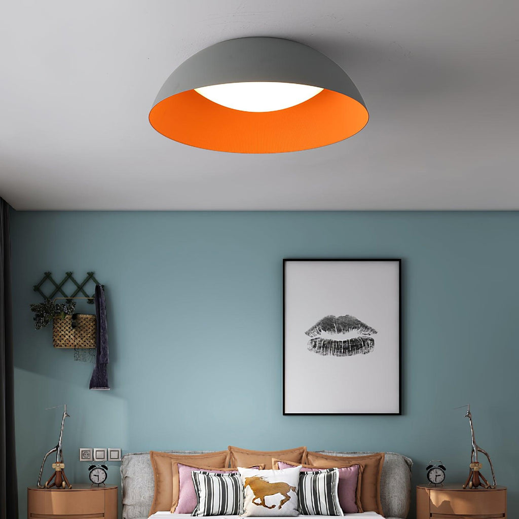 Grey dome ceiling light from Clérachic with an orange inner rim, above a bed against a blue-green wall with a lips print.