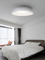 White low dome ceiling light from Clérachic above a bedroom with white bedding, sheer curtains and an orange lounge chair.