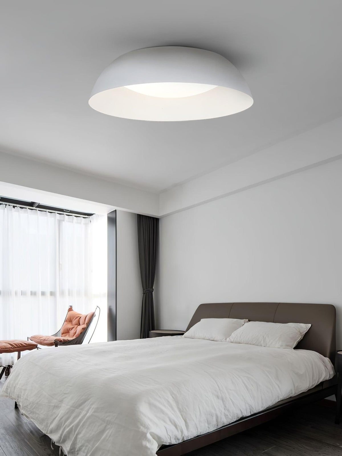White low dome ceiling light from Clérachic above a bedroom with white bedding, sheer curtains and an orange lounge chair.
