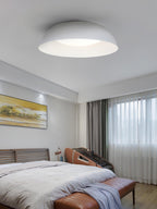 Low white dome ceiling light above a bedroom with a slatted bed, an orange bench and a painting, from Clérachic.
