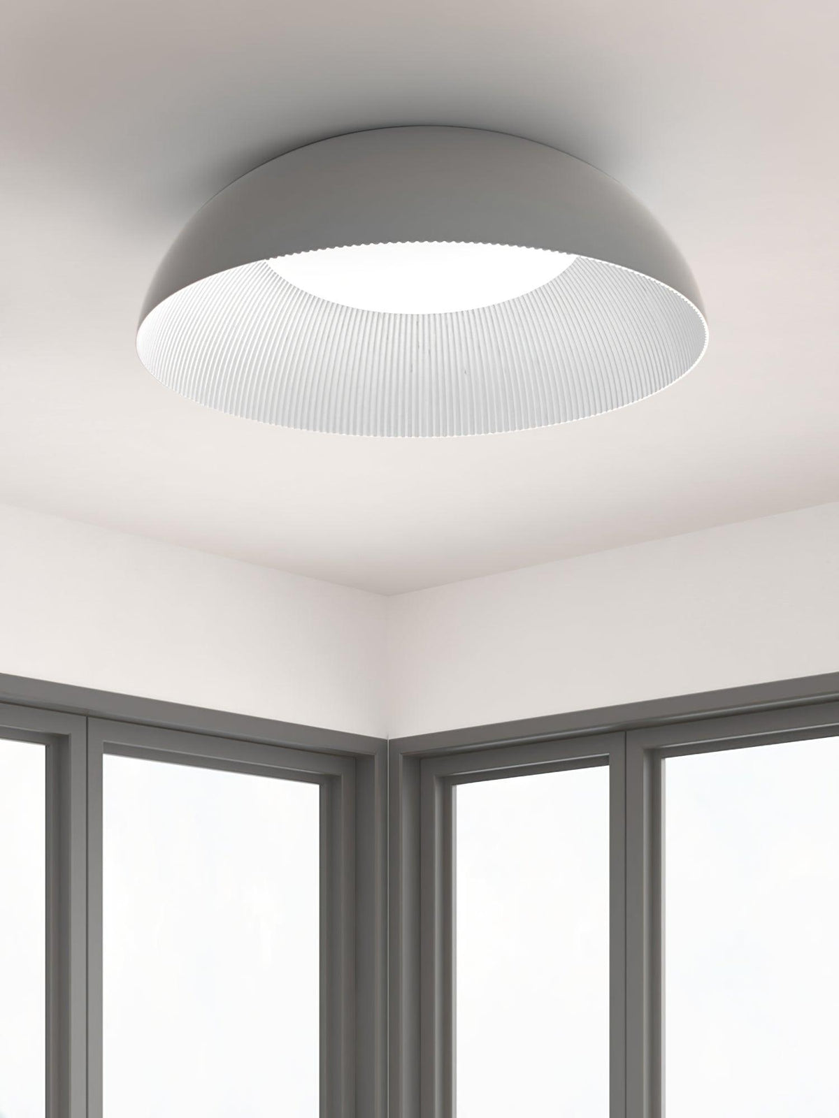 Grey outer shell and ribbed white inner rim of this Clérachic ceiling light, seen from below in a corner of a room with tall windows.