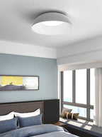 Grey dome ceiling light with a white interior above a bedroom with navy bedding, a window seat and a landscape print, from Clérachic.