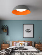 Grey dome with orange inner rim over a bed with striped cushions and a horse pillow, against a blue wall, from Clérachic.