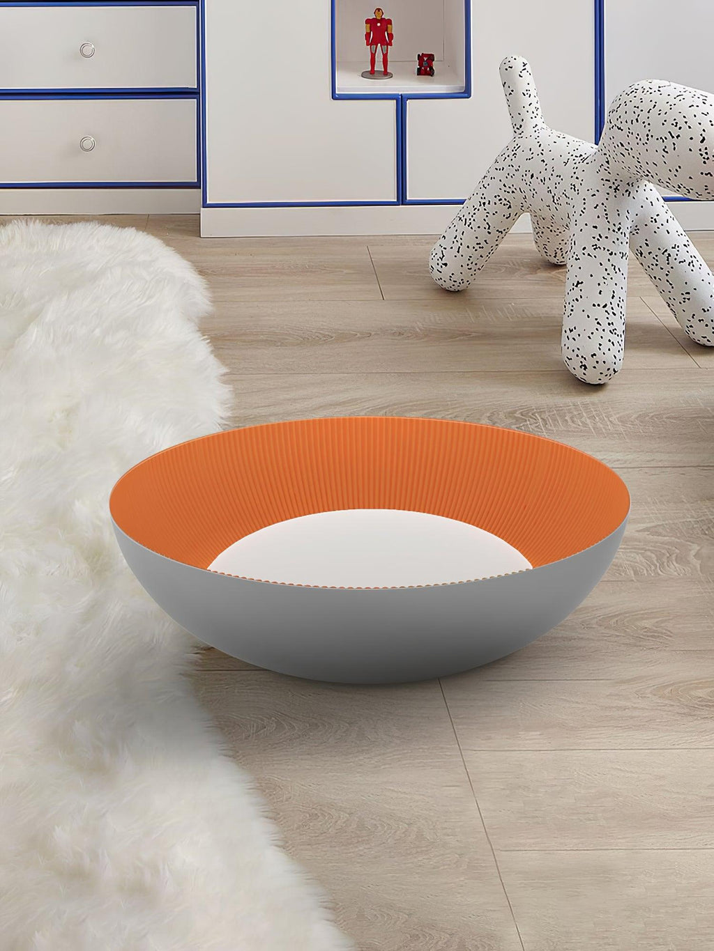 Grey bowl with an orange ribbed inside and a white centre resting on a wood floor beside a fluffy rug and a spotted dog sculpture, from Clérachic.