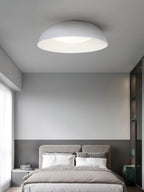 White low dome ceiling light from Clérachic above a bedroom with a taupe headboard, white pillows and a grey half-painted wall.
