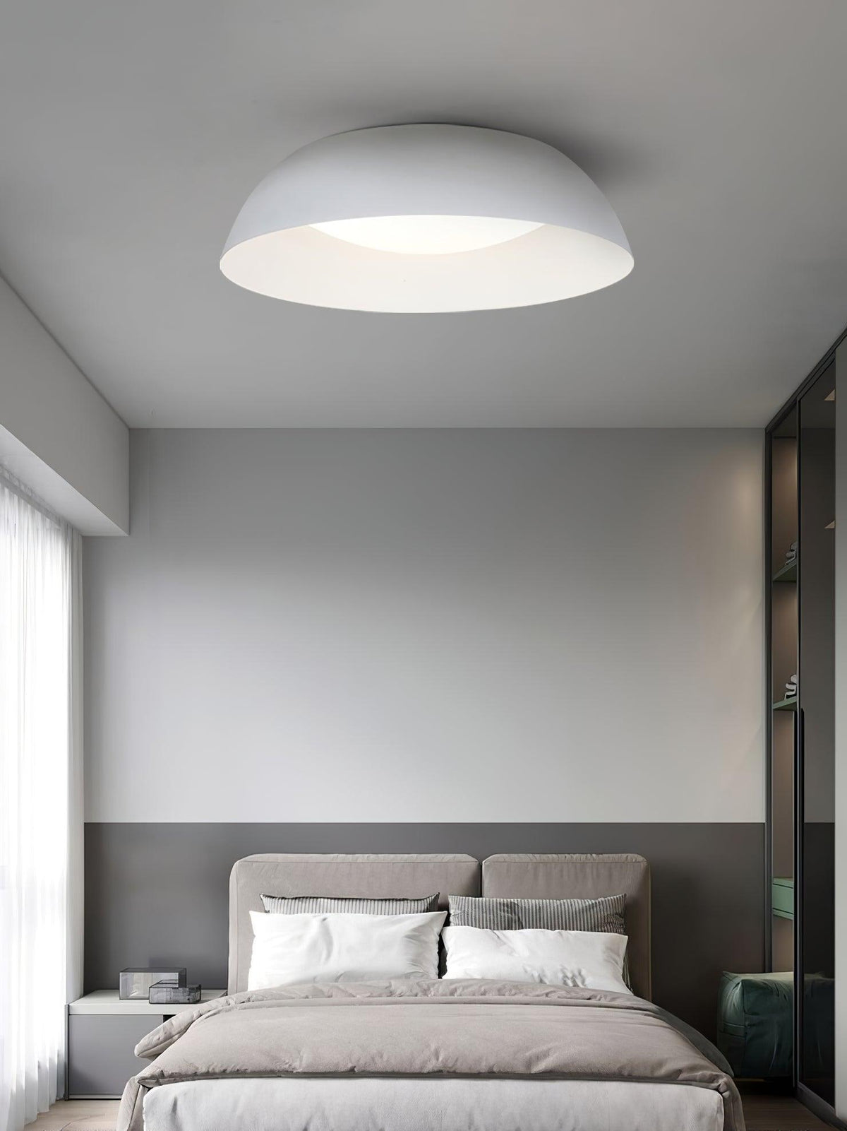 White low dome ceiling light from Clérachic above a bedroom with a taupe headboard, white pillows and a grey half-painted wall.