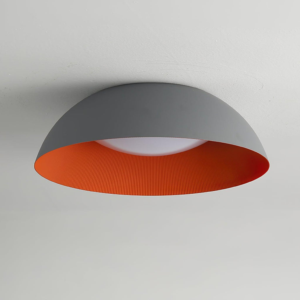 Grey dome ceiling light with an orange ribbed interior and a white diffuser, photographed from below on a pale ceiling, from Clérachic.