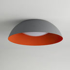 Grey dome ceiling light with an orange ribbed interior and a white diffuser, photographed from below on a pale ceiling, from Clérachic.