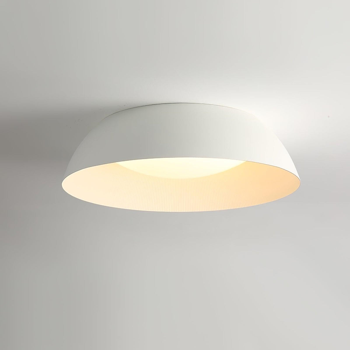 White dome ceiling light from Clérachic lit softly, its inner rim glowing cream, photographed from below.