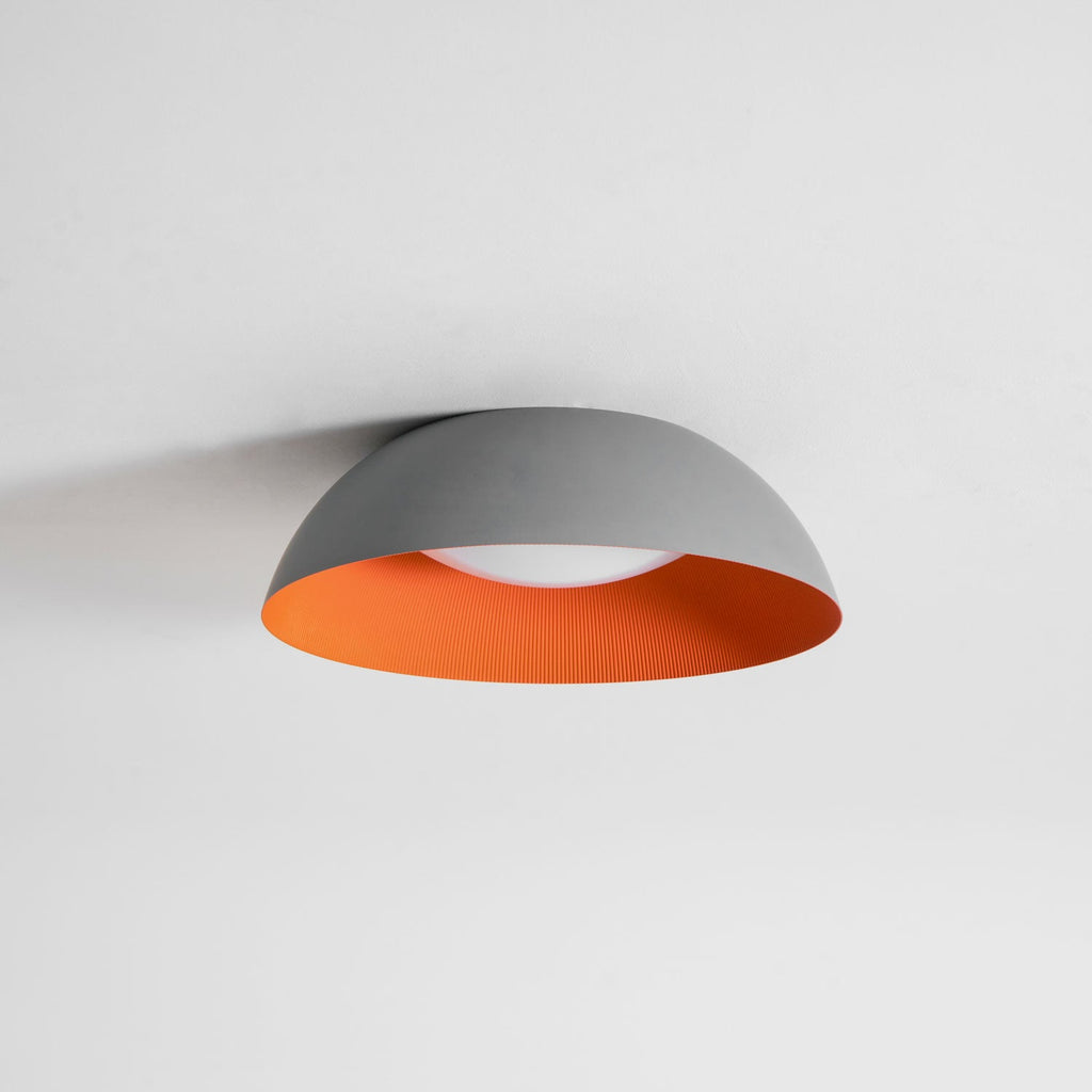 Grey dome ceiling light with an orange interior and a white diffuser, from Clérachic, on a plain pale ceiling.