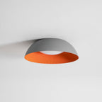 Grey dome ceiling light with an orange interior and a white diffuser, from Clérachic, on a plain pale ceiling.