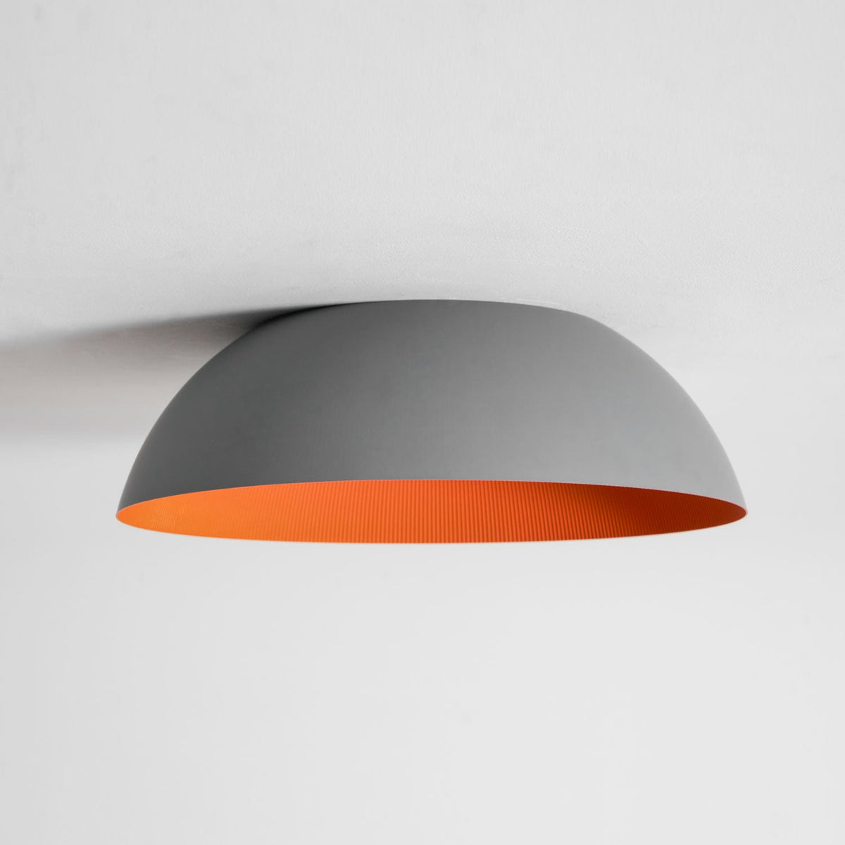 Grey dome ceiling light from Clérachic seen from the side, with a thin band of orange visible along the lower edge.