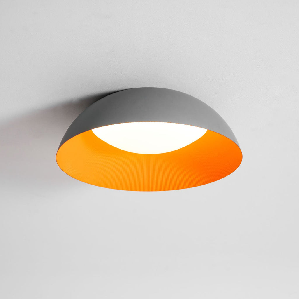 Grey dome ceiling light with an orange interior and a lit white diffuser, from Clérachic, shown on a light ceiling.