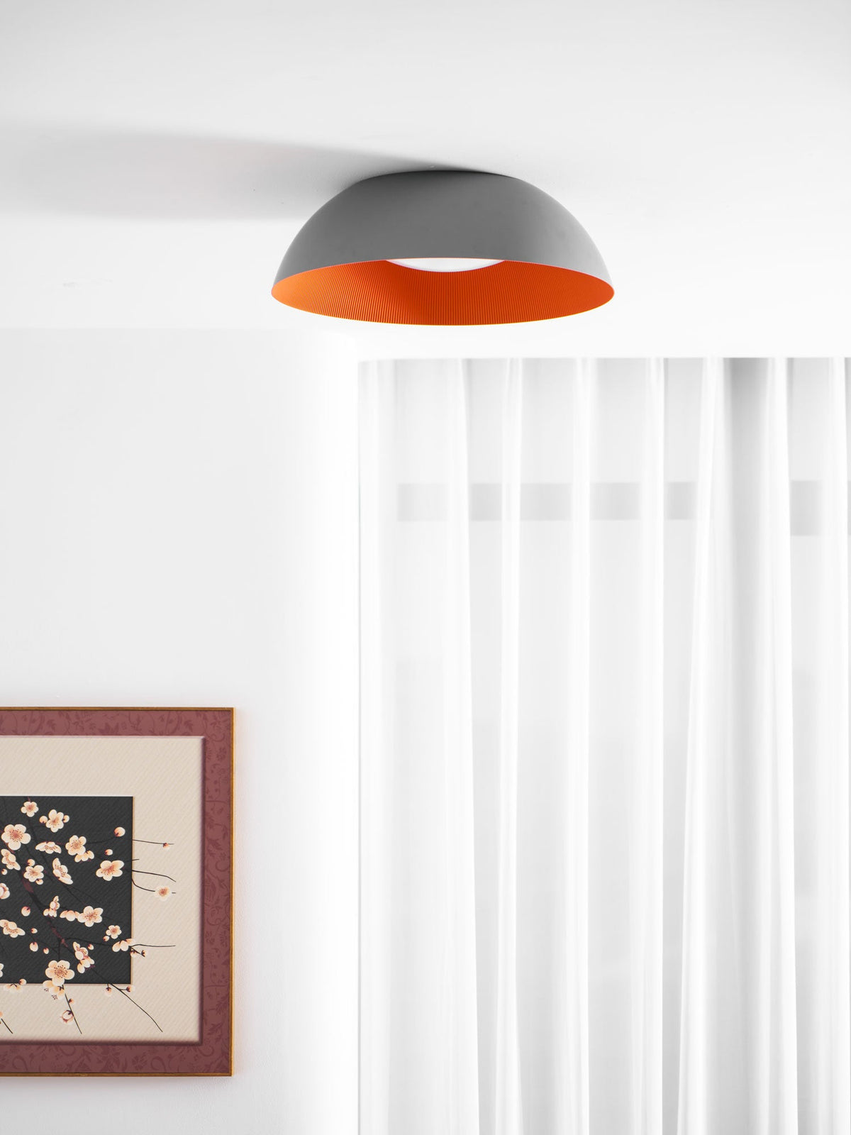 Grey and orange dome ceiling light from Clérachic in a white room with sheer curtains and a framed floral print at the edge.
