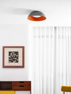 Grey dome with orange inner rim seen from below in a white room with sheer curtains, a framed print and a sideboard, from Clérachic.